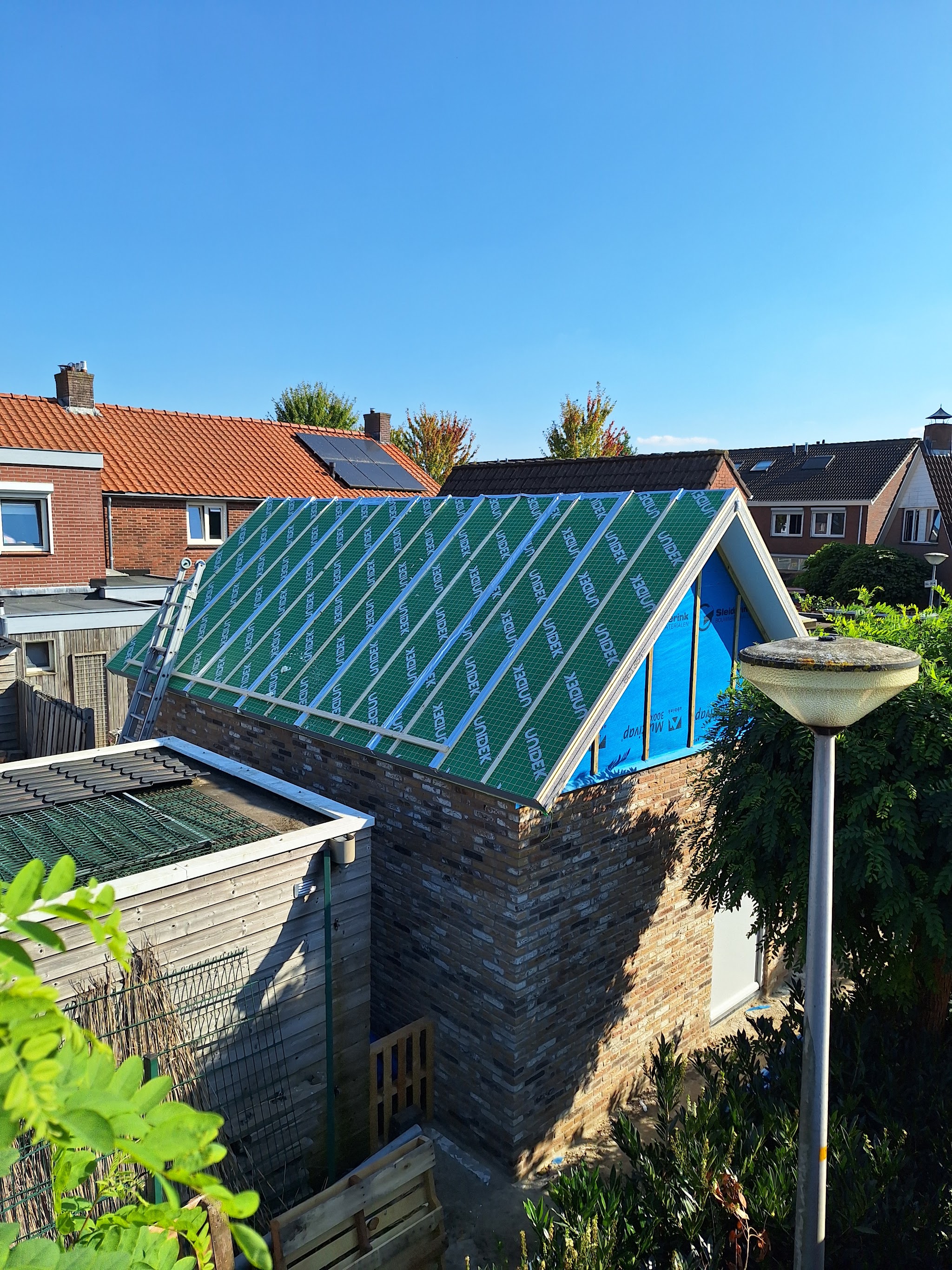 Dakconstructie van een bijgebouw met dampopen folie onder een blauwe lucht