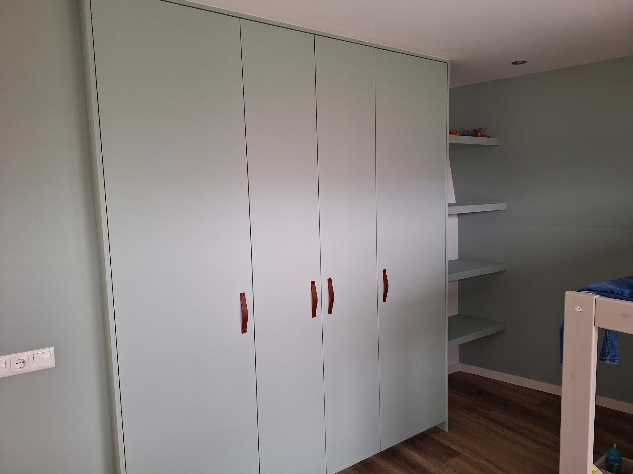 Groene inbouwkast met rode grepen in een kinderkamer